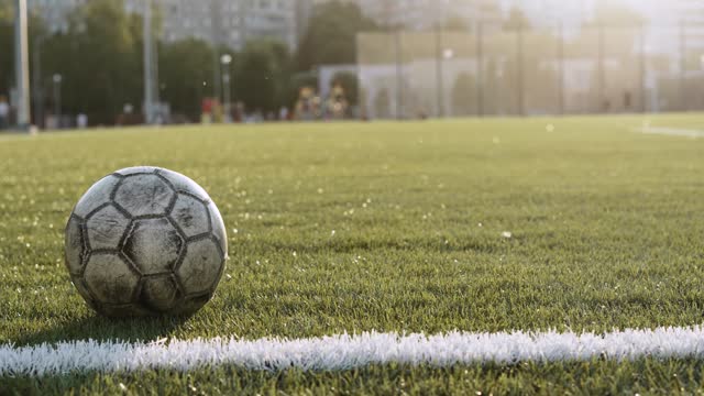 Old gray soccer ball slowly rolls along white line of football field.