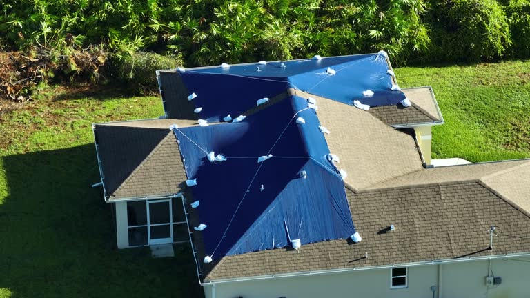 Hurricane Ian damaged house rooftop covered with protective plastic tarp against rain water leaking until replacement of asphalt shingles. Aftermath of natural disaster