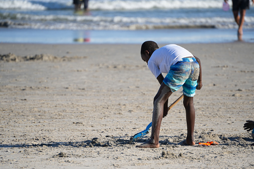 Black boy with a shovel plays in beach sand of Atlantic City, NY on September 15th, 2023