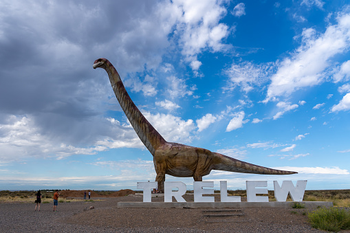 Chubut Province, Argentina - January 20, 2023: Visitors watching the replica of Titanosaurus with Trelew sign near Museo Paleontologico Egidio Feruglio (MEF) in Trelew, Chubut Province, Argentina.