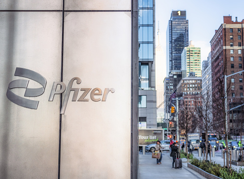 New York City, USA - A Pfizer sign outside their headquarters building in Midtown Manhattan, with pedestrians and traffic on the street beyond.