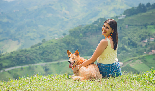 a woman and her dog sit on the edge of a mountain outdoors and look at the camera