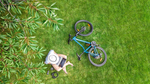 istock Young woman using laptop computer in park, student girl freelancer working and studying online outdoors sitting on grass with bicycle and laptop, aerial drone view from above 1689066470