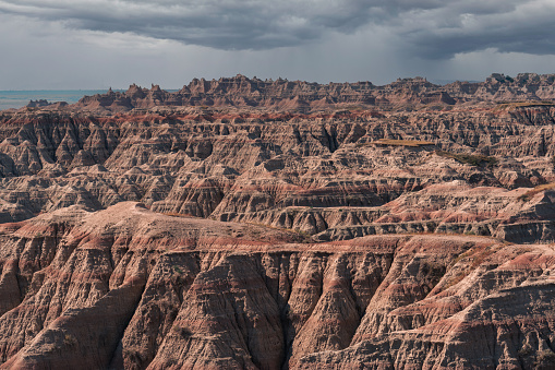 Rugged dirt and rock hills rise over a green grassed valley in the Badlands National Park in South Dakota.