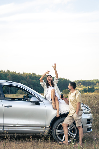 Happy man and woman enjoy a summer weekend picnic with a car outside the city in a field on a sunny day, sunset, vacation and trip, copy space.