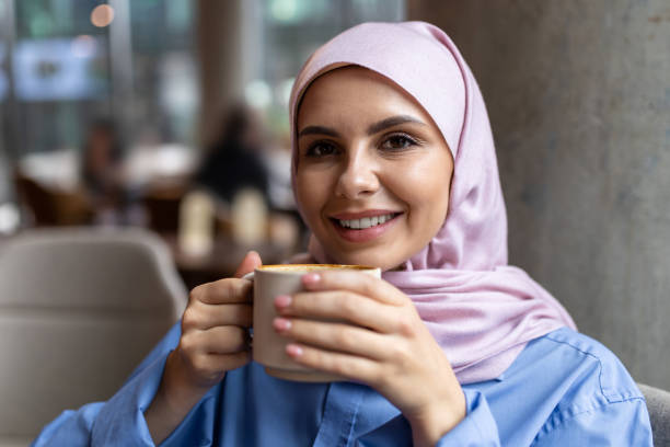 istock Woman in pink hijab drinking coffee and smiling 1689100707