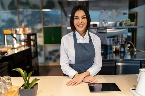 Coffee shop. Cute dark-haired coffee shop assistant with a tablet in hand smiling nicely