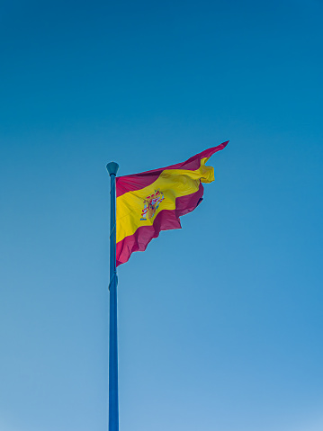 flagpole with the flag of Spain fluttering in the wind, with a background of blue sky, copy space