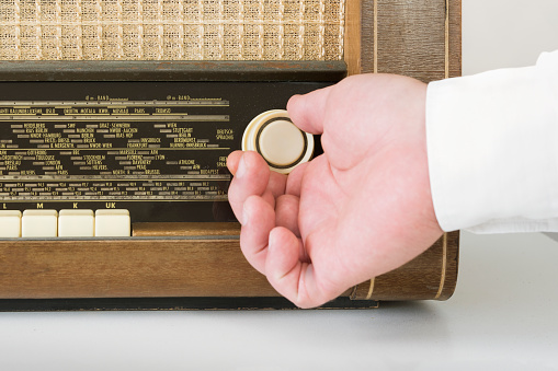 Authentic 60s radio receiver. Front view. On white background. Traces of time. A man's hand on the wave setting radio knob. Close-up