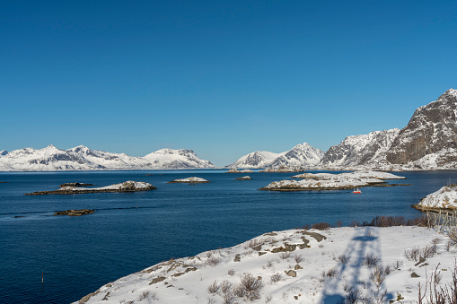 Small island around fishing village Henningsvær in the Lofoten Island on sunny winter day against rocky mountain.