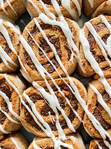 Stock photo showing a tray containing homemade, wholemeal cinnamon swirl danish pastries drizzled with icing.