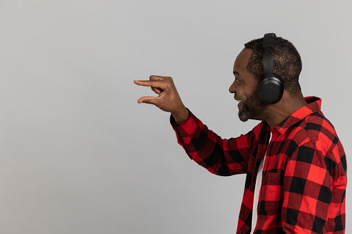Happy black bearded man in headphones wearing red checkered shirt showing small size posing isolated over gray studio background.