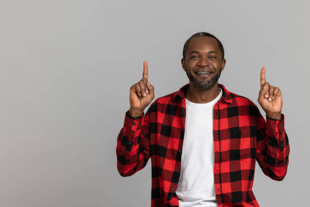 istock Cheerful black bearded man wearing red checkered shirt pointing up at copy space for advertisement 1689151643