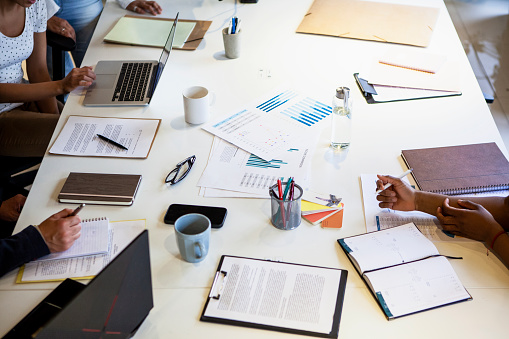 High angle view of boardroom table with coworkers using laptop and discussing project over paperwork