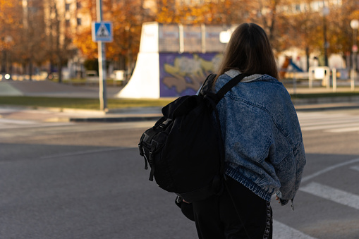 Rear view of unrecognizable teenage girl with backpack walking on street. A Young woman walks down city street, black backpack on his back.