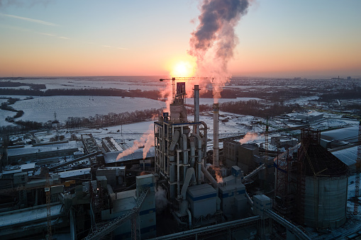 Aerial view of cement factory tower with high concrete plant structure at industrial production area at sunset. Manufacturing and global industry concept.