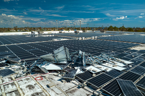 Photovoltaic solar panels destroyed by hurricane strong wind mounted on industrial building roof for producing green ecological electricity. Consequences of natural disaster in Florida.