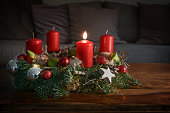 Advent wreath with one burning red candle and Christmas decoration on a wooden table in front of the couch, festive home decor for the first Sunday, copy space, selected focus