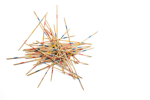Mikado game on white, wooden pick-up sticks should be taken without moving the others, metaphor in business to solve one problem after another without endangering the whole, copy space, selected focus