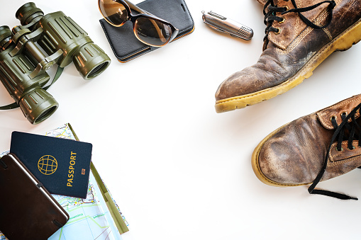 Trekking boots, binoculars, passport and other accessories for hiking vacation, flat lay on a light background, copy space, selected focus