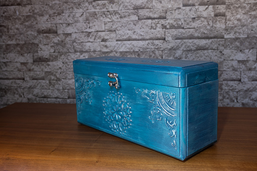 Blue colored wooden chest with embossed lace embroidery in front of brick patterned background