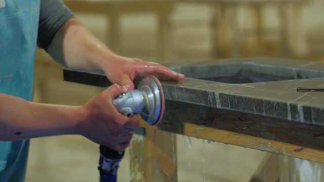 worker polishing edge of granite kitchen countertop - quartz -rock with a polisher with water in a warehouse. United States
