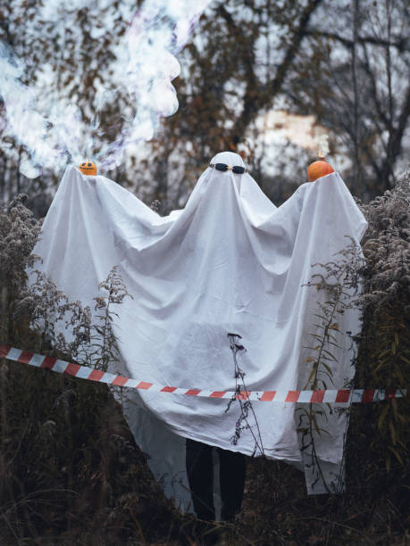 istock Halloween ghost costume made from a bed sheet, holding pumpkin bombs in his hands. 1689373441