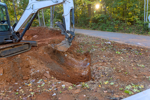 Worker uses a tractor to excavate ditch for laying drainage conduit