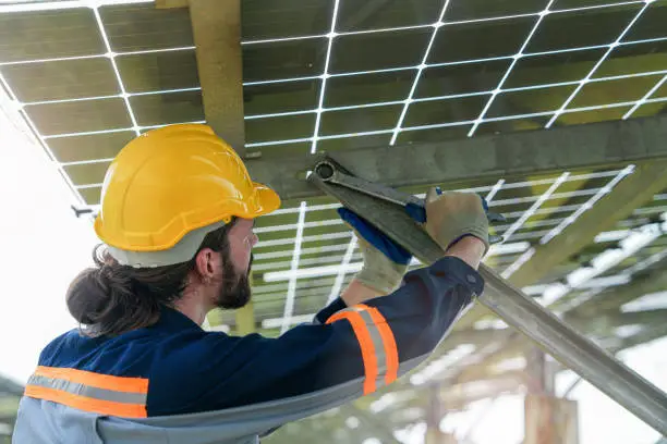 Factory engineer man checking and repairing solar panel construction. Worker works at solar farm for renewable energy. Solar cell industry for sustainability.
