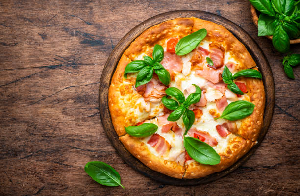 istock Hot pizza with ham, pancetta, mozzarella cheese, tomato sauce and green basil, rustic wooden table background, top view 1689672956