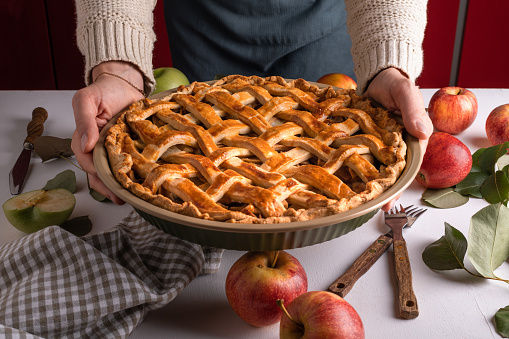 Woman holding and showing tasty cooked apple pie ready to be putting in the oven. Thanksgiving tart preparation, autumn bakery. Crispy weather sweets. Recipe