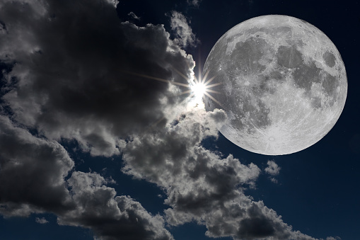 Close-up photo looking up at a large full moon partially covered by clouds. Copy space.