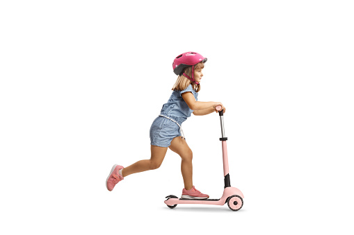 Full length shot of a girl with helmet riding a pink scooter isolated on white background