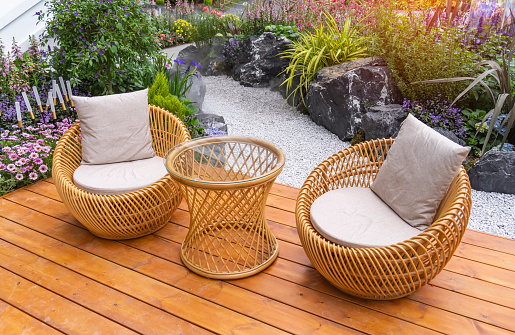 Garden decorated with outdoor wicker furniture and growing flowers in pots. fresh blooming potted plants for summer entertainment visits