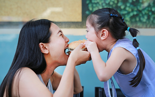 Mother and her daughter eating hamburger together.