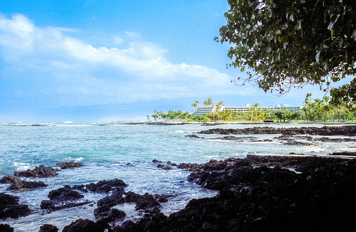 Vintage 1980s film photograph of the lava fields of black volcano rock against the blue waters of the ocean on the tropical island of Maui, Hawaii.