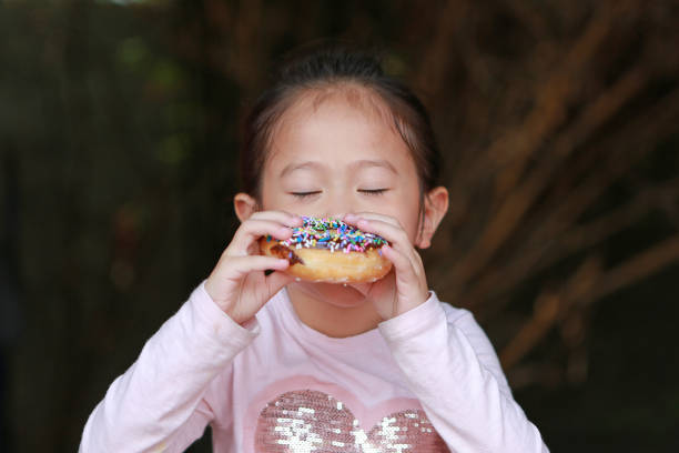 Close up Asian child girl enjoy eating rainbow donut.