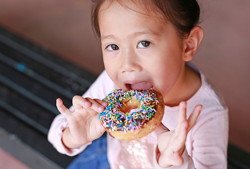 Cute Asian child girl enjoy eating rainbow donut.