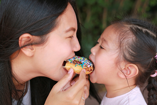 Close up Asian mother and her daughter eating rainbow donut together.