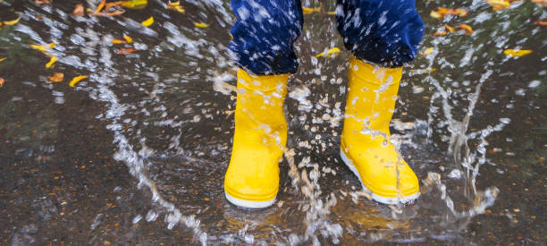 istock Kid jumping in the puddle. Rubber waterproof yellow boots. Banner 1689902288