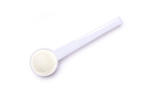 Powdered milk or milk powder in plastic spoon isolated on white background. Clipping path. Top view, flat lay.