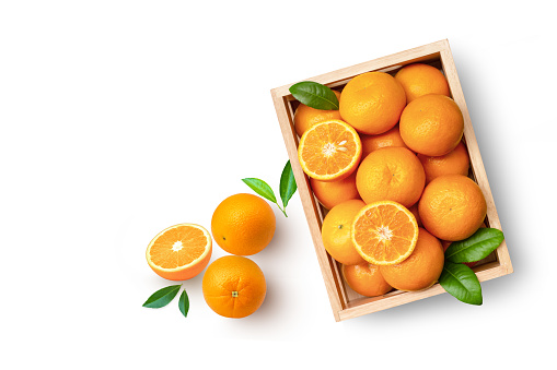 Orange fruit with half slice and green leaves in wooden box isolated on white background with copy space, top view, flat lay.