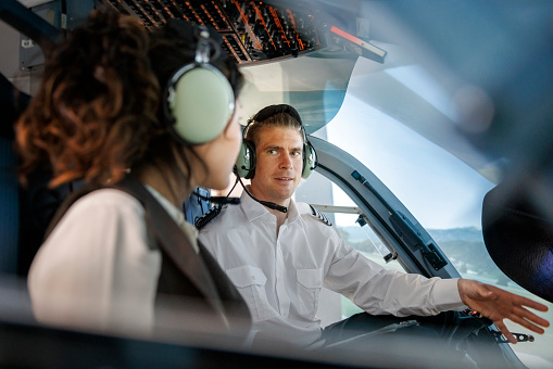 Male pilot talking with woman trainee pilot sitting inside a flight simulator. Pilot explaining how a flight simulator works to a female student during a training session in a aviation academy.