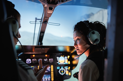 Rear view of a female trainee pilot listening to instructor during a flight simulation training. Woman learning to fly helicopter with instructor inside a flight simulator.