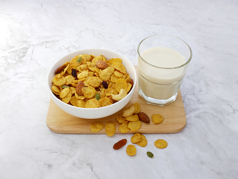 Grains cornflakes in bowl with milk glass on marble background.