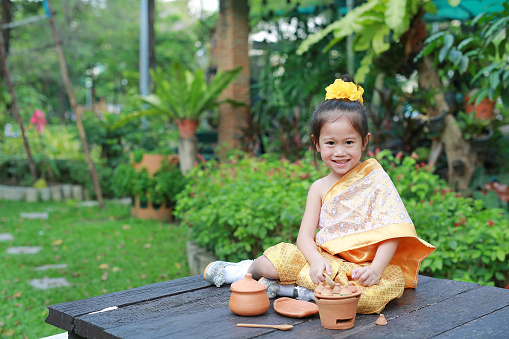 Beautiful Asian child girl in traditional thai dress play making Thai culture dessert in the public garden.