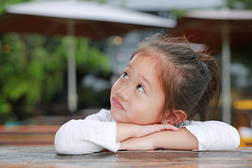 Adorable little Asian kid girl with funny face with looking up lying on the wooden table.