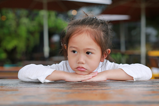 Adorable little Asian child girl expressed disappointment or displeasure on the wood table with looking out.
