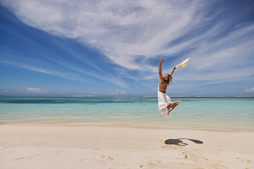 Back view of smiling woman having fun while jumping in summer day on the beach. Copy space.