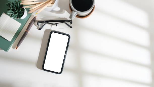 istock Top view smart phone with empty screen, notebook and coffee cup on wooden office desk. Copy space for your text. 1690019052